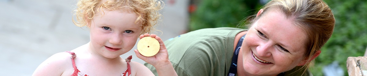 A little girl proudly shows off a gold coin she has found during one of our summer family activities as a member of our Learning Team looks on and smiles